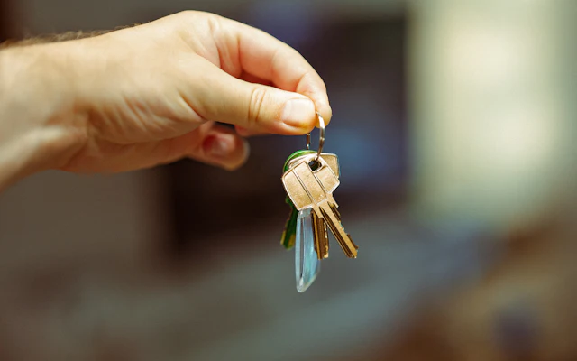 A hand holding up a small bunch of brass keys on a ring, with a blurred room behind